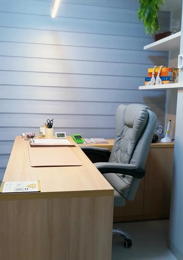Consultório com mesa de madeira, cadeira e estante com plantas
